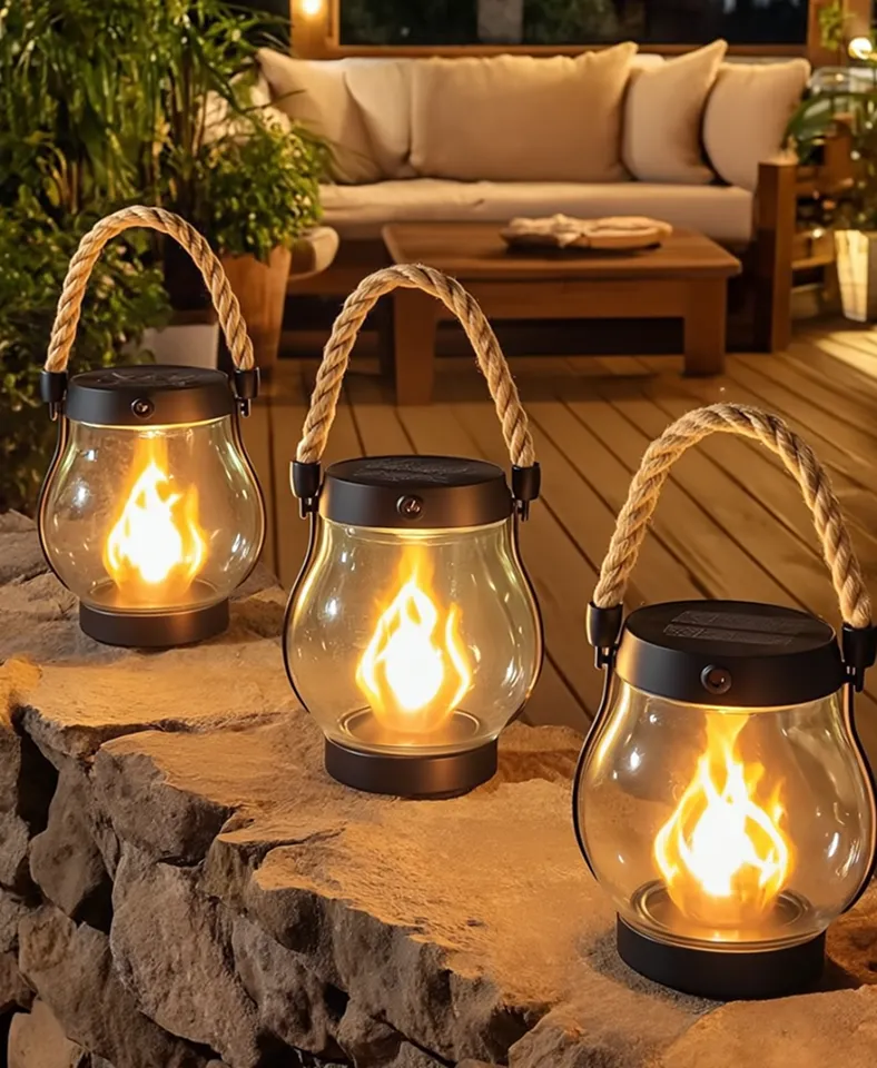 Three lanterns with glowing flames on a stone ledge with a cozy patio setup.