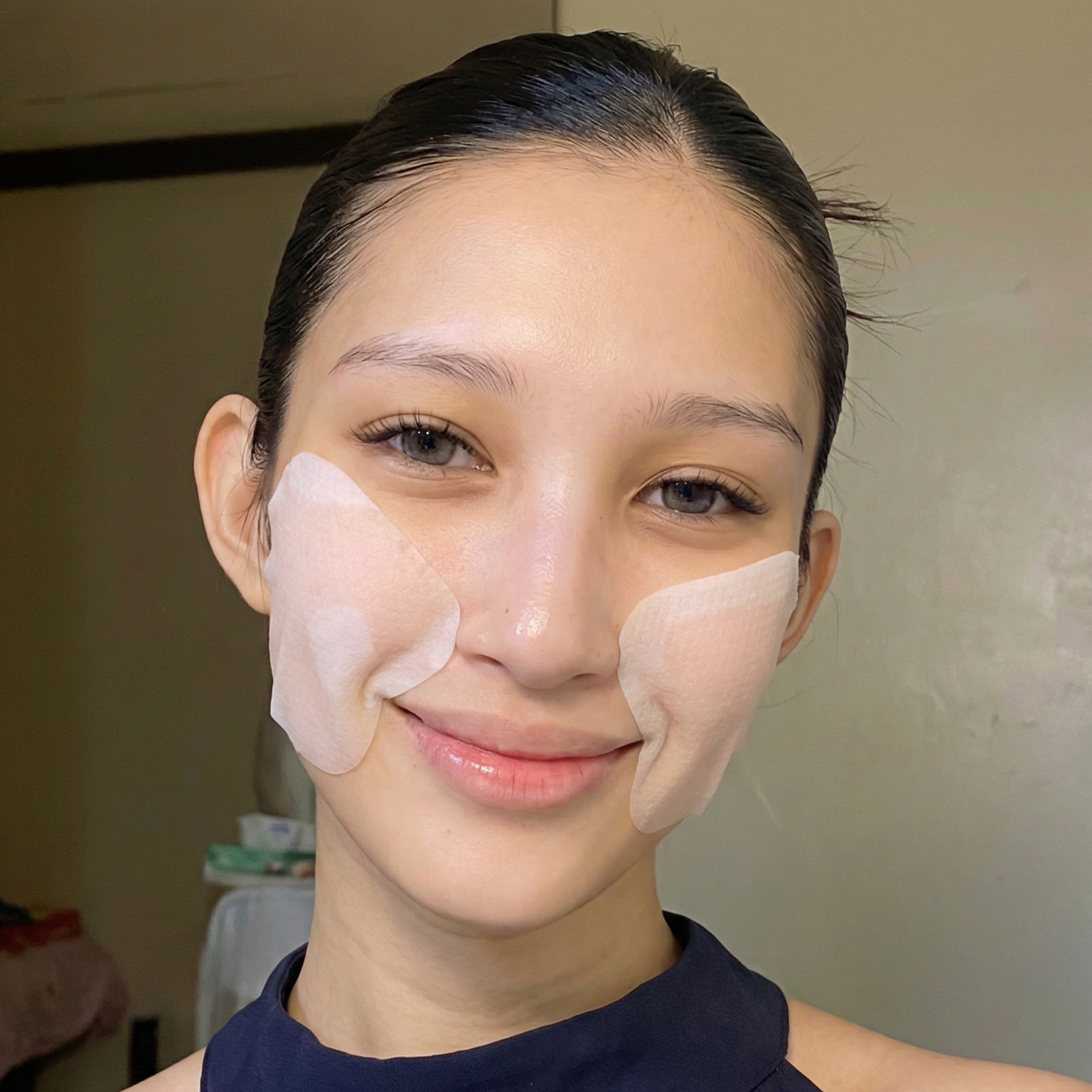 A smiling young woman with her hair pulled back and white skincare patches on her cheeks.