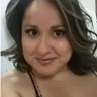 A close-up photo of a woman with wavy brown hair and brown eyes, smiling slightly at the camera.