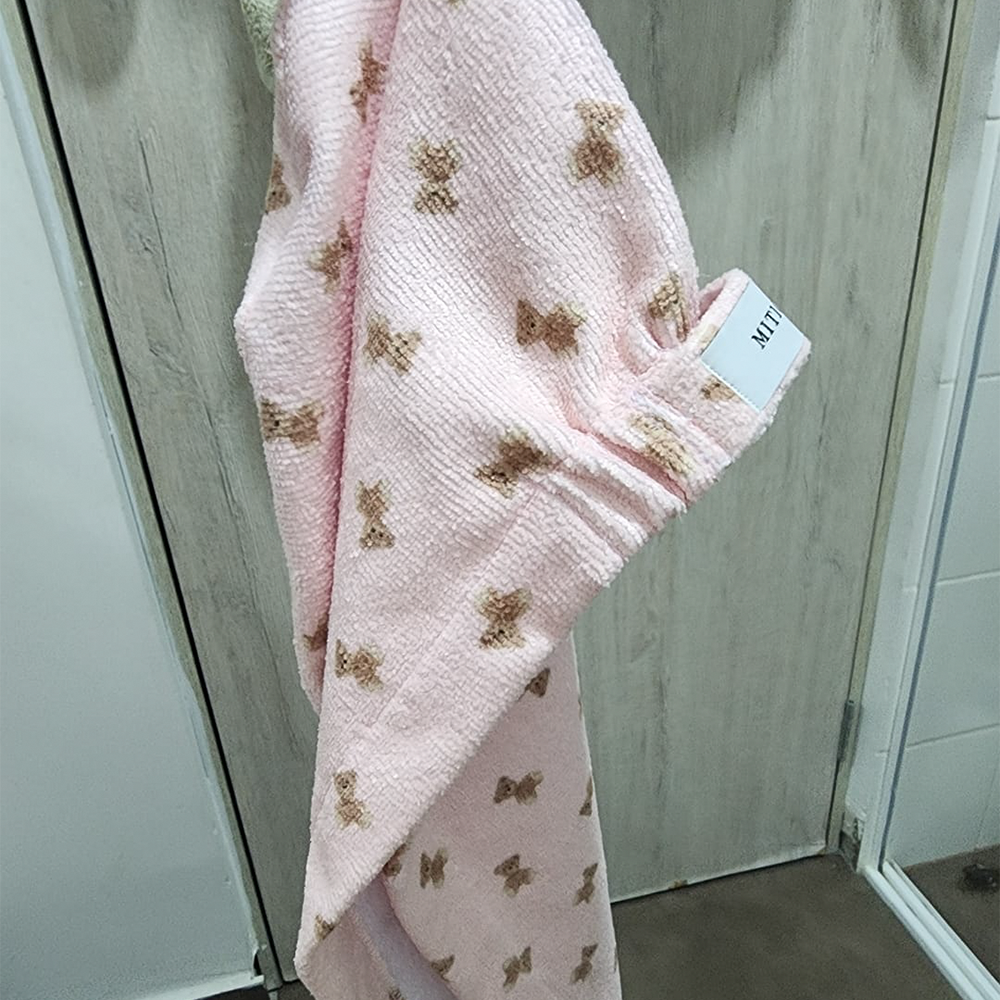 Hanging pink towel with brown bear patterns on a wooden door.