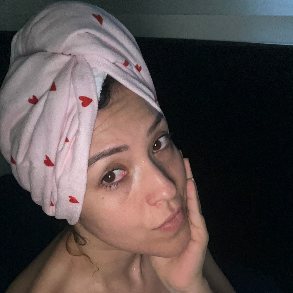Person with towel wrapped around head, touching face gently, in dim lighting.