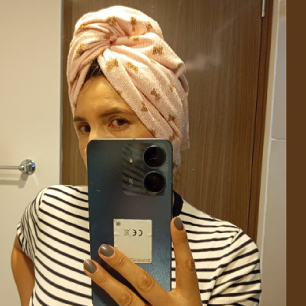 Person in striped shirt and towel taking a mirror selfie with phone.