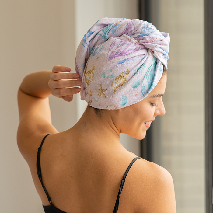 Person with a towel wrapped on their head, standing by a window.