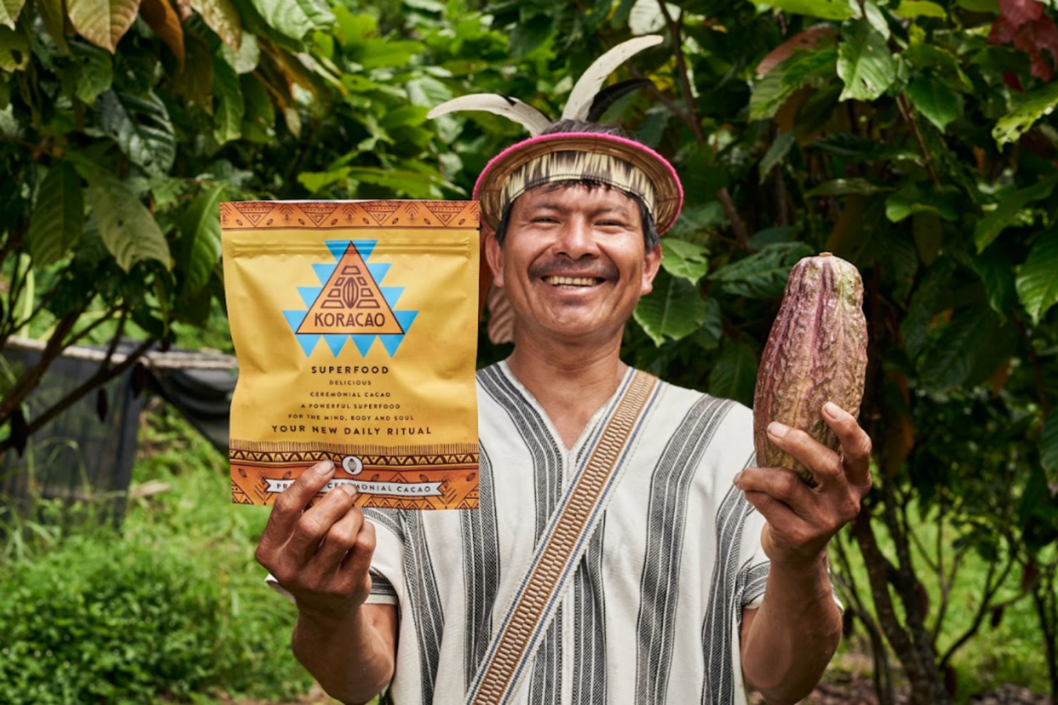 Smiling man holding cacao pod and Koracao superfood package in a garden.