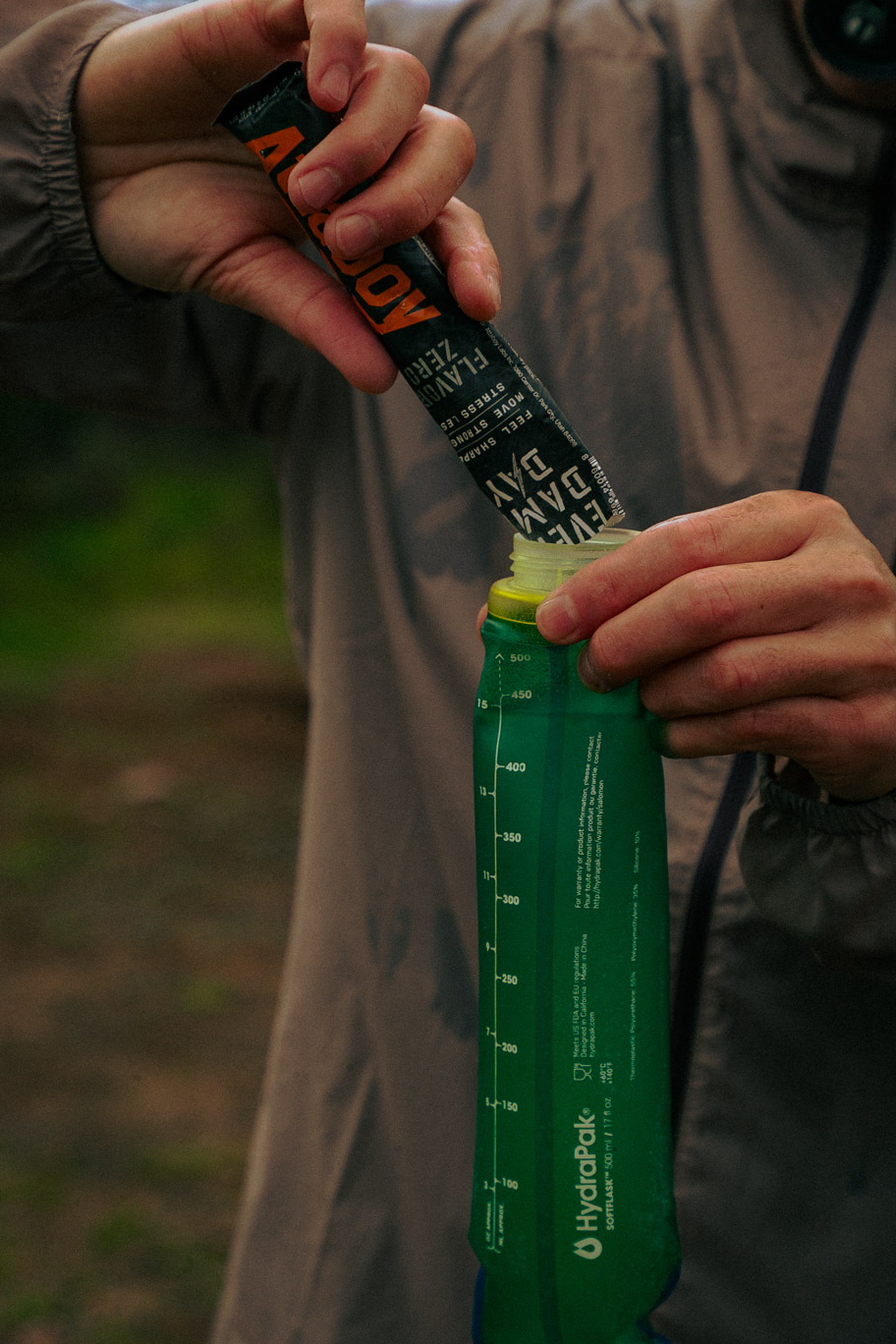A person's hands pouring the contents of a stick pack into a green HydraPak soft flask.