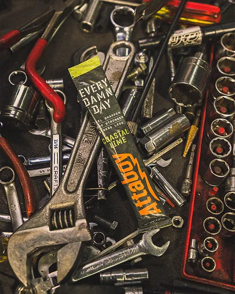 An 'Attaboy' energy packet lying on top of various tools in a cluttered toolbox drawer.