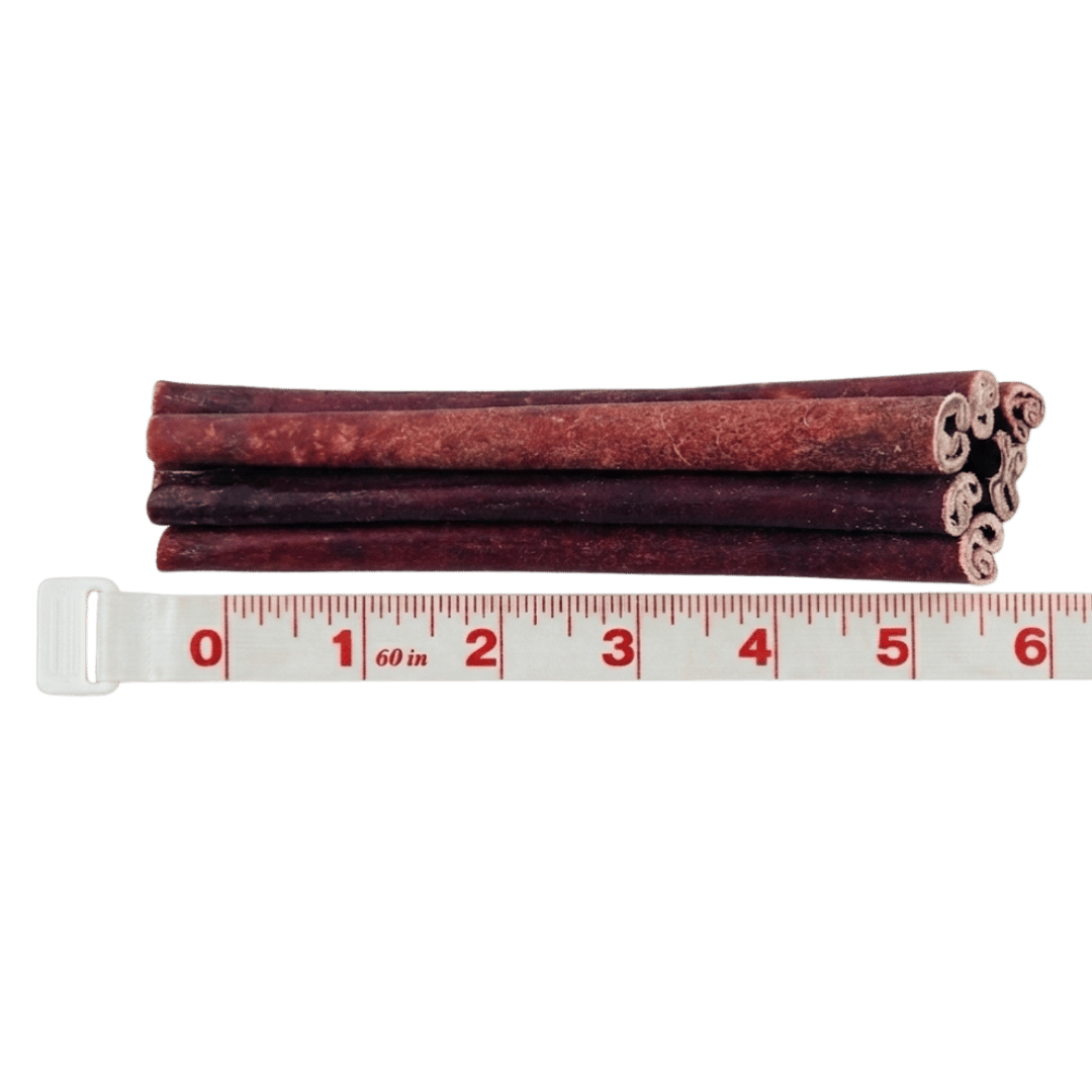 A stack of reddish-brown rolled dog chews measured against a tape measure, showing a length of six inches.