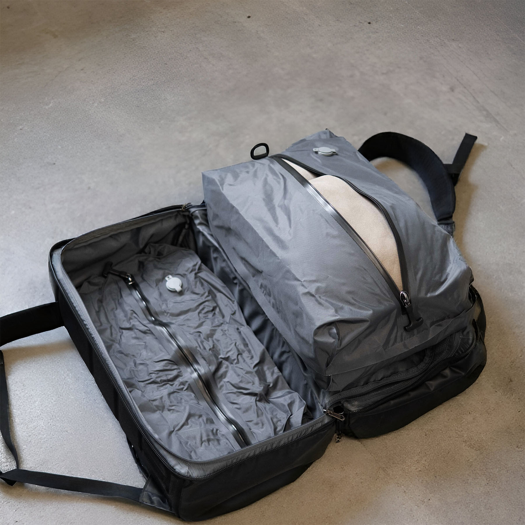 Open gray travel bag with compartments on a concrete floor.