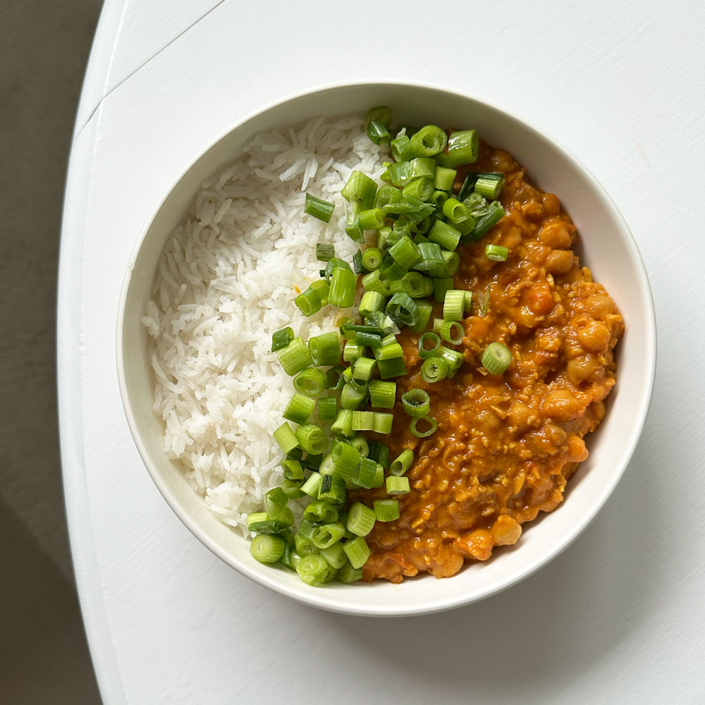 A white bowl filled with rice and a chickpea stew, topped with chopped green onions.