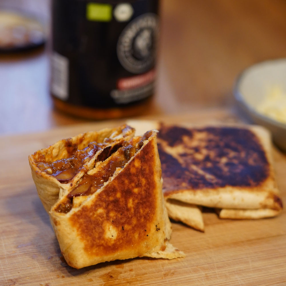 A close-up of a toasted wrap, cut in half to show the filling, on a wooden board.