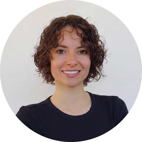 A headshot of a smiling woman with short, curly brown hair, wearing a black shirt against a white background.