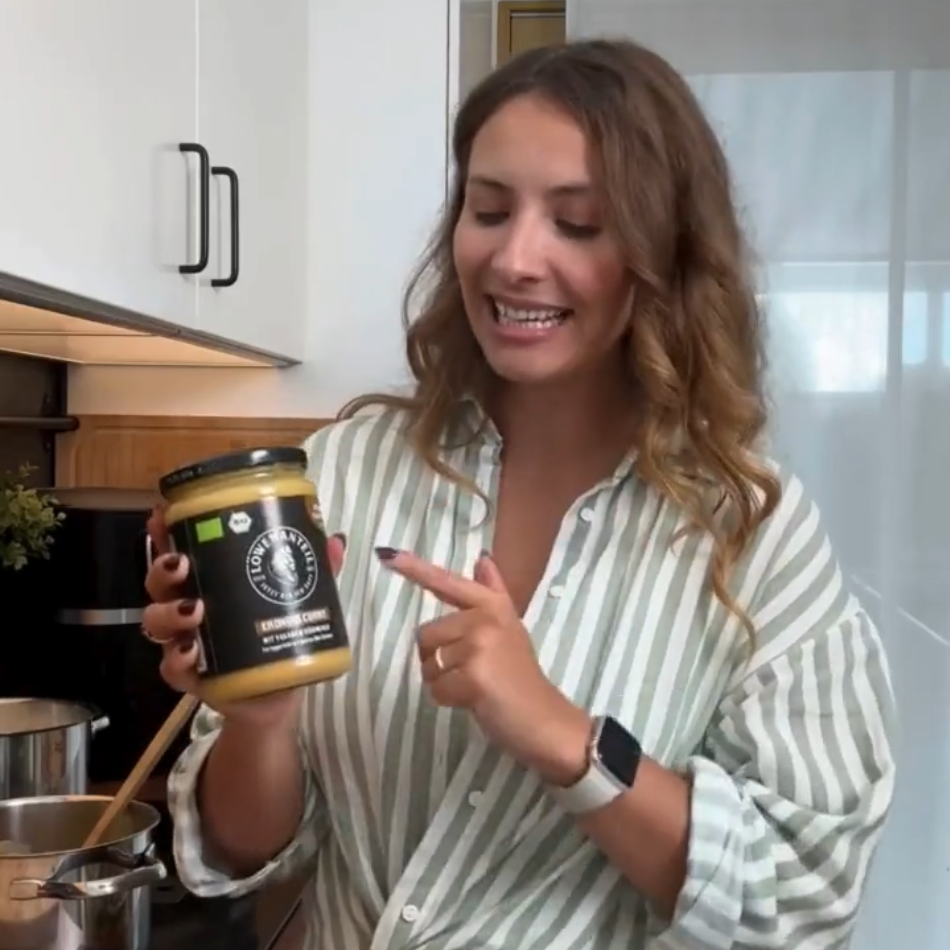 A woman in a striped shirt stands in a kitchen, holding and pointing to a jar of food.