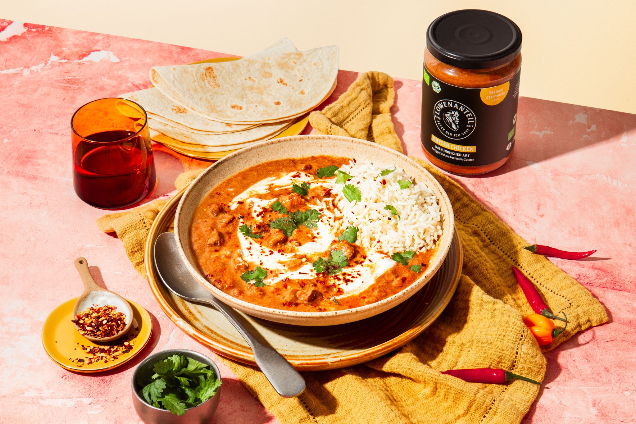 Bowl of curry with rice, tortillas, chili flakes, fresh cilantro, and a jar of sauce.