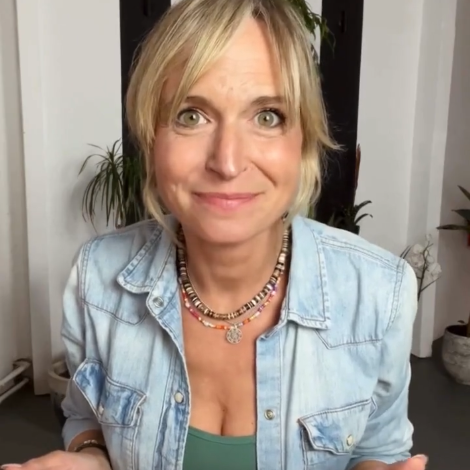 A woman with blonde hair and a denim shirt smiles while looking at the camera.