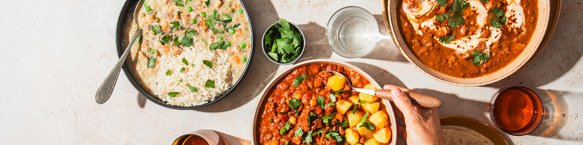 An overhead view of a table set with several bowls of stews and curries with garnishes.
