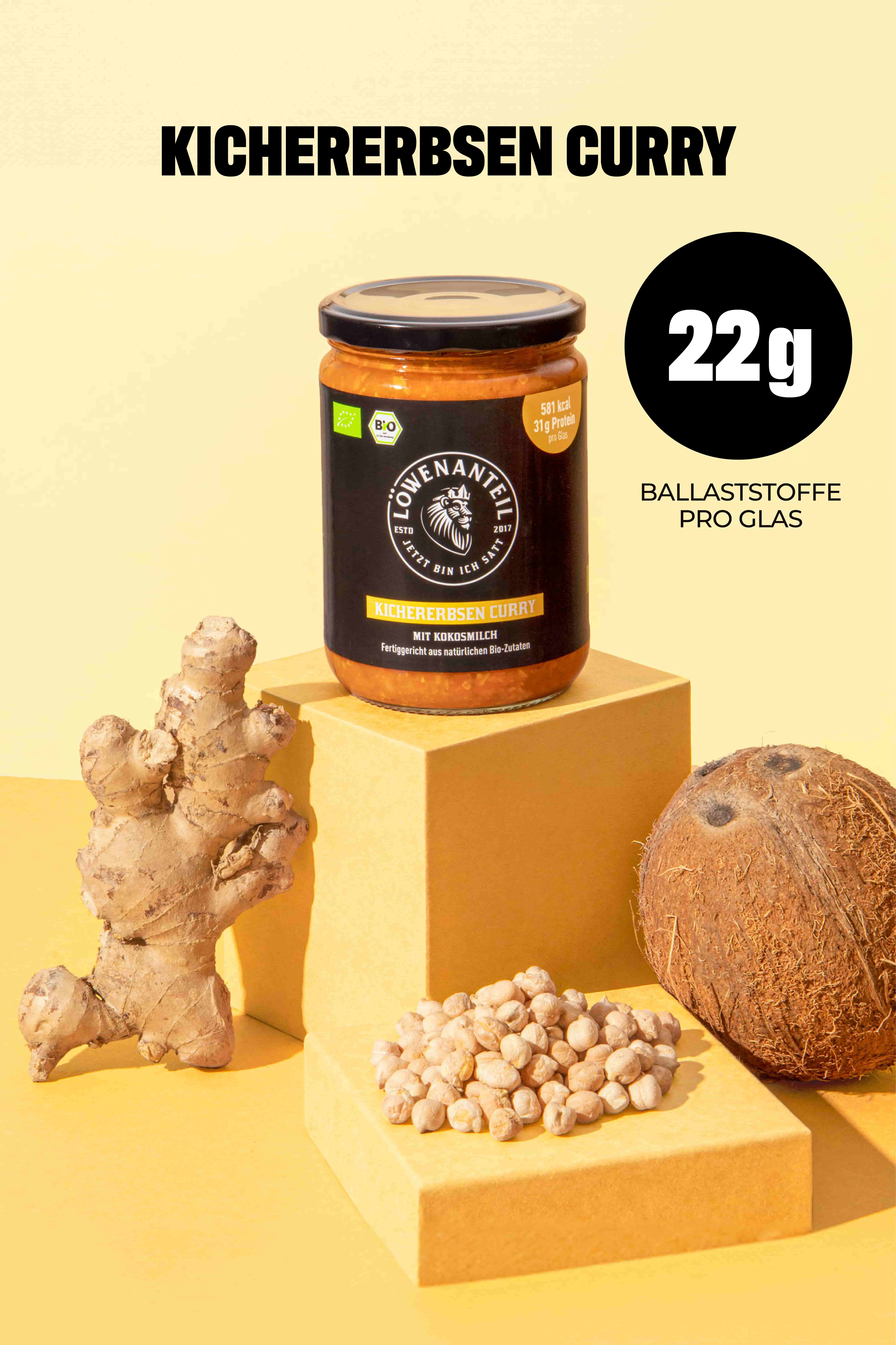 A jar of chickpea curry sits on yellow blocks, surrounded by ginger, a coconut, and chickpeas.