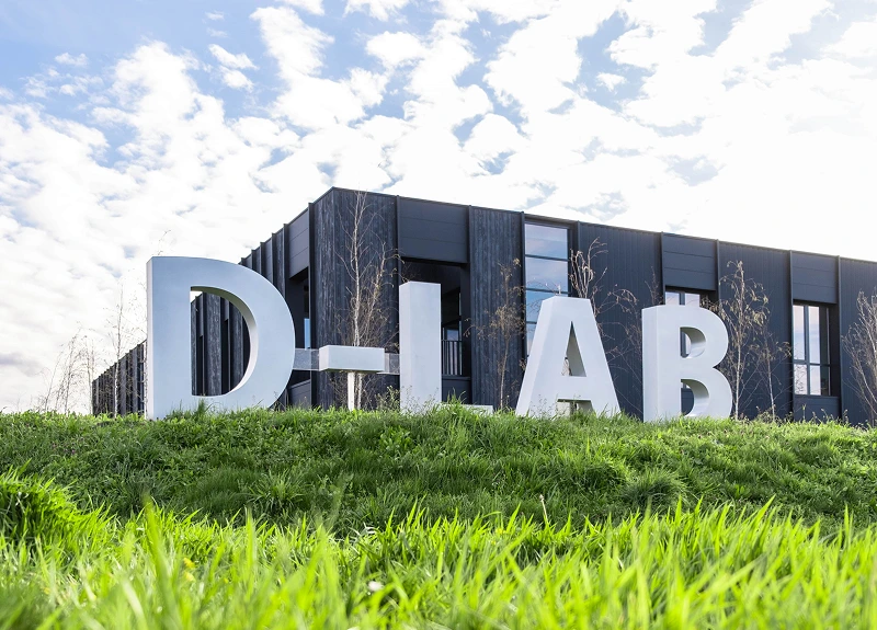 Large 'D-LAB' letters in front of a modern building with a grassy foreground.