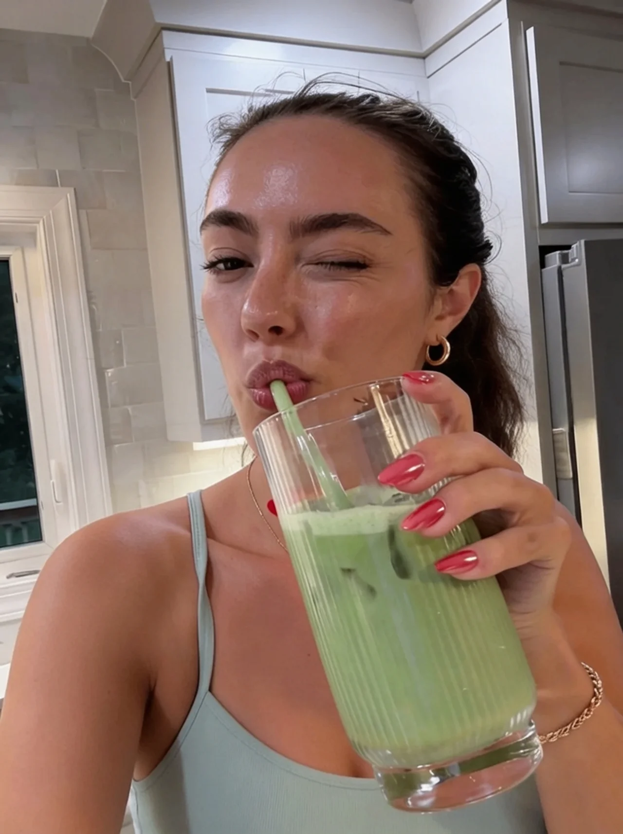 A smiling woman holds a green pouch of YVIA Matcha Collagen Vanilla next to a black tumbler.
