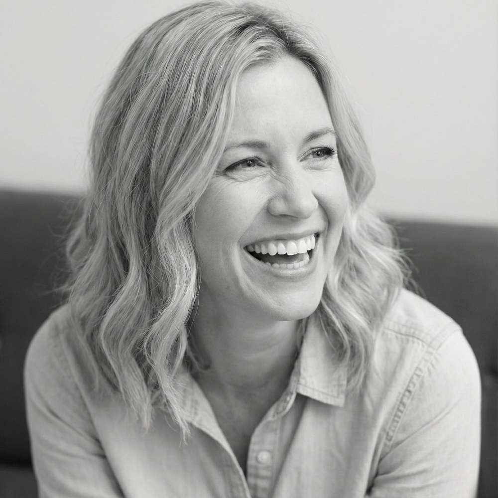 A black and white headshot of a woman with wavy blonde hair laughing and looking to the side.