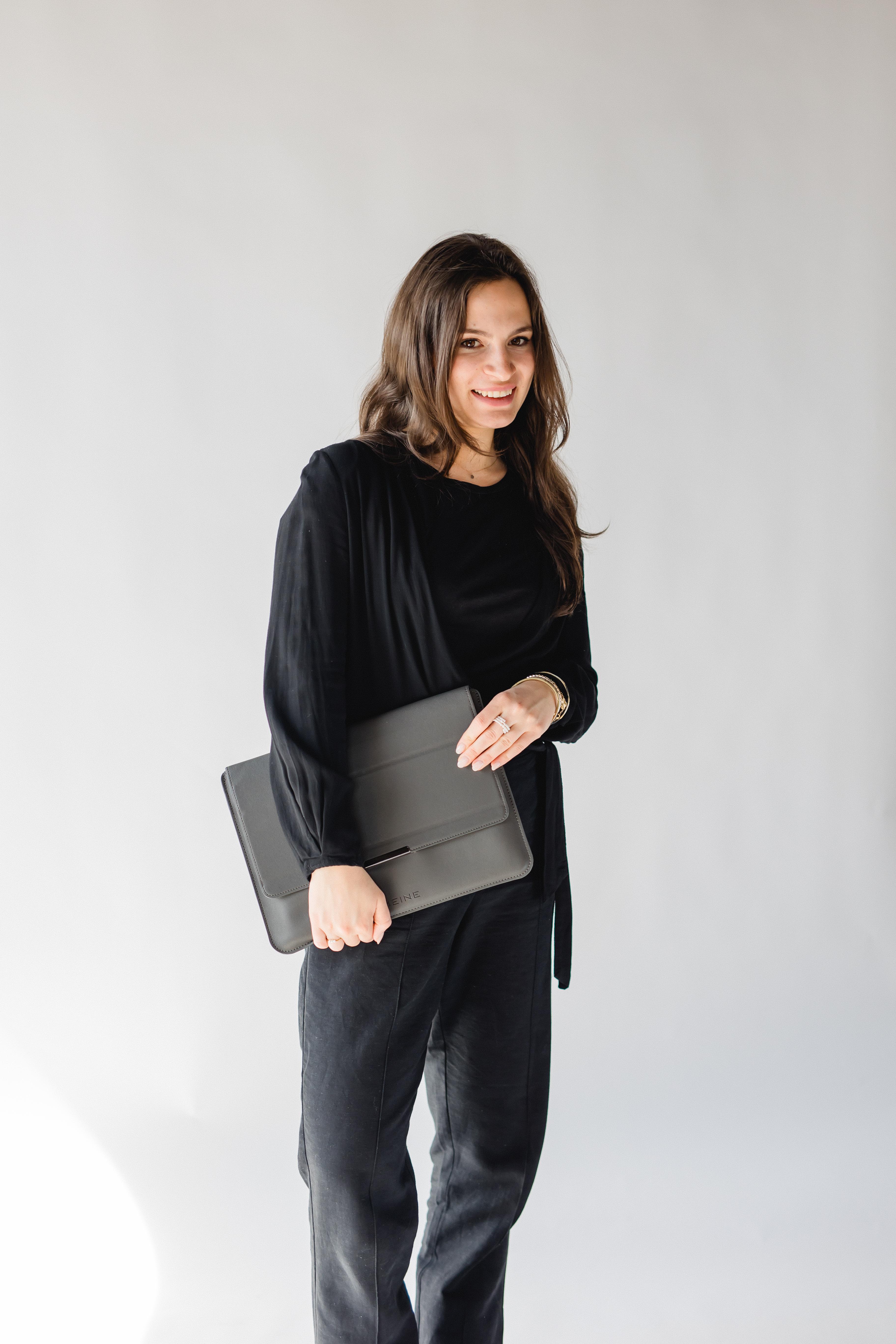 Smiling woman in black holding a folder on a light background.