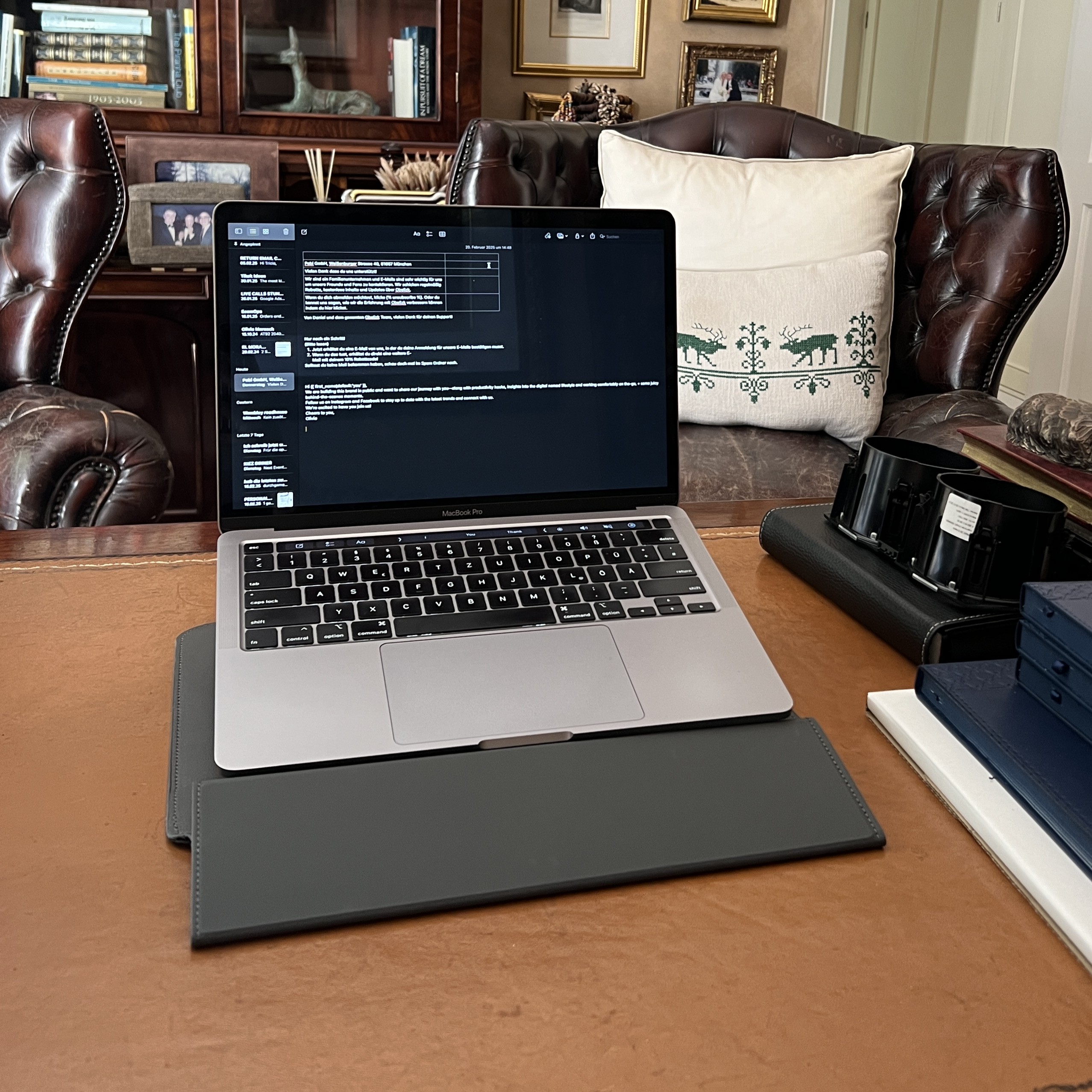 A laptop on a desk in an office with leather chairs.
