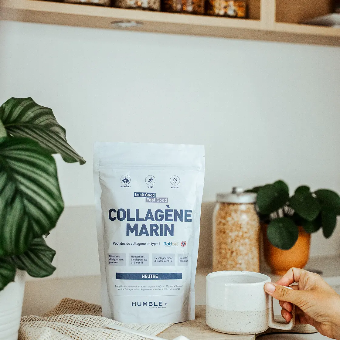 A pouch of Humble+ Marine Collagen on a kitchen counter next to a mug held by a hand.