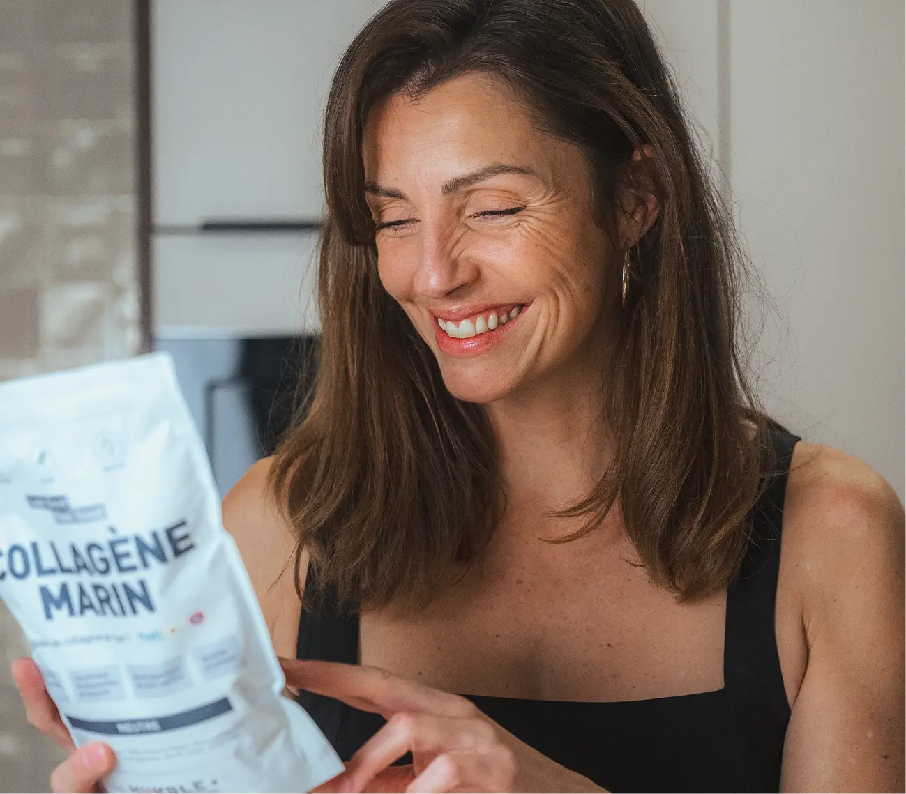 A smiling woman with her eyes closed holds a white pouch of 'Collagène Marin'.