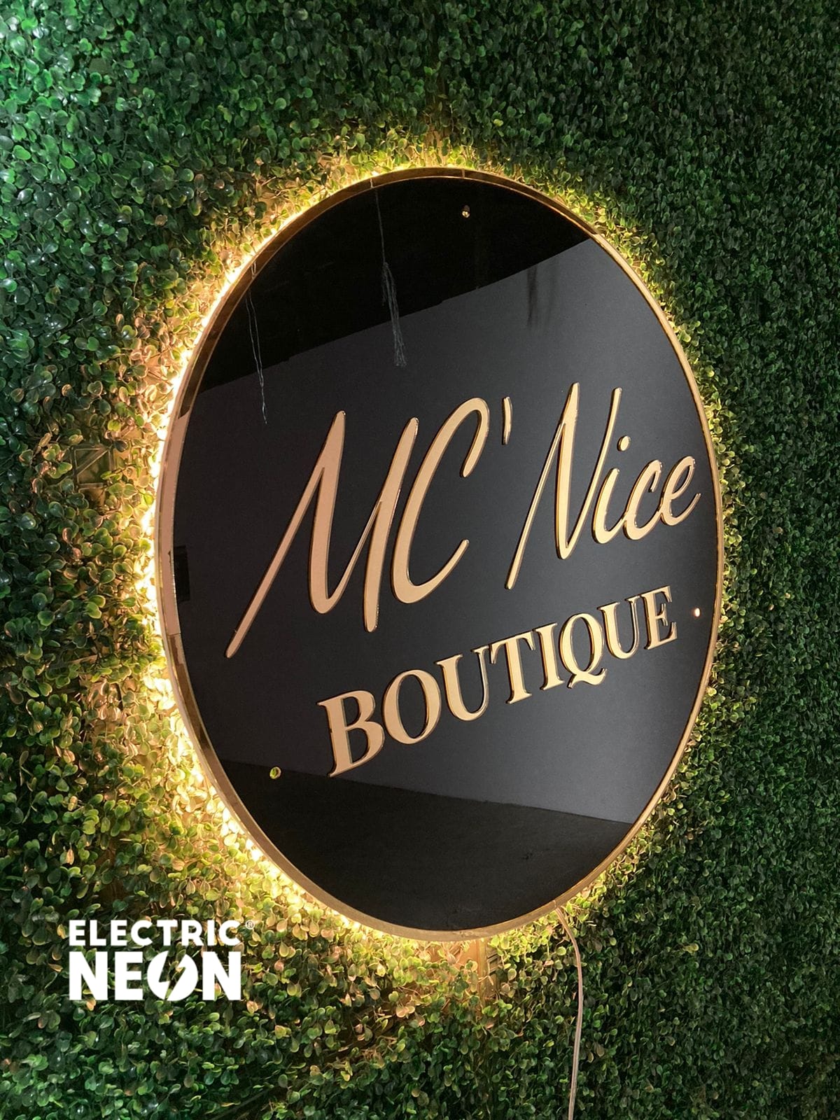 Round sign with 'MC' Nice Boutique' on a leafy green wall.