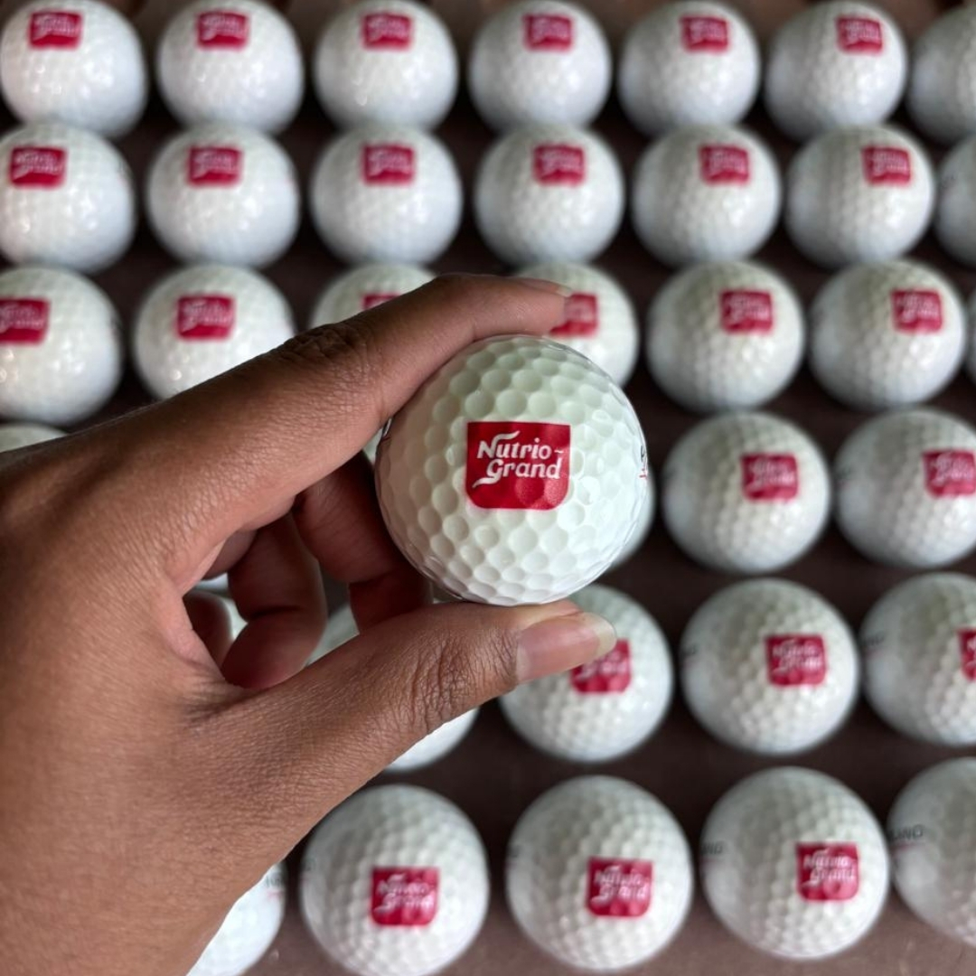 Hand holding a golf ball with 'Nutrio Grand' logo among many others.