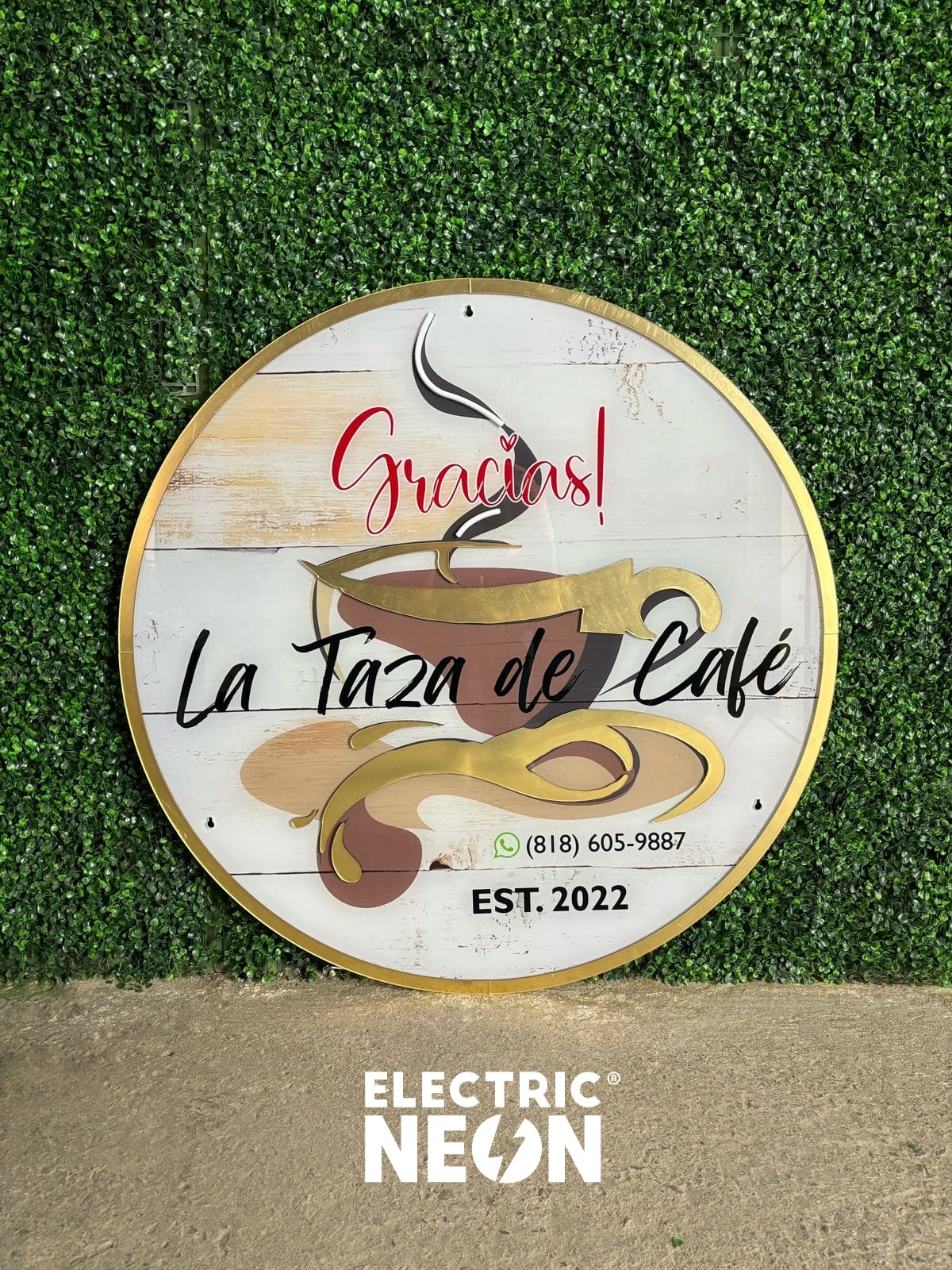 Round sign with 'Gracias! La Taza de Café' on green foliage background.