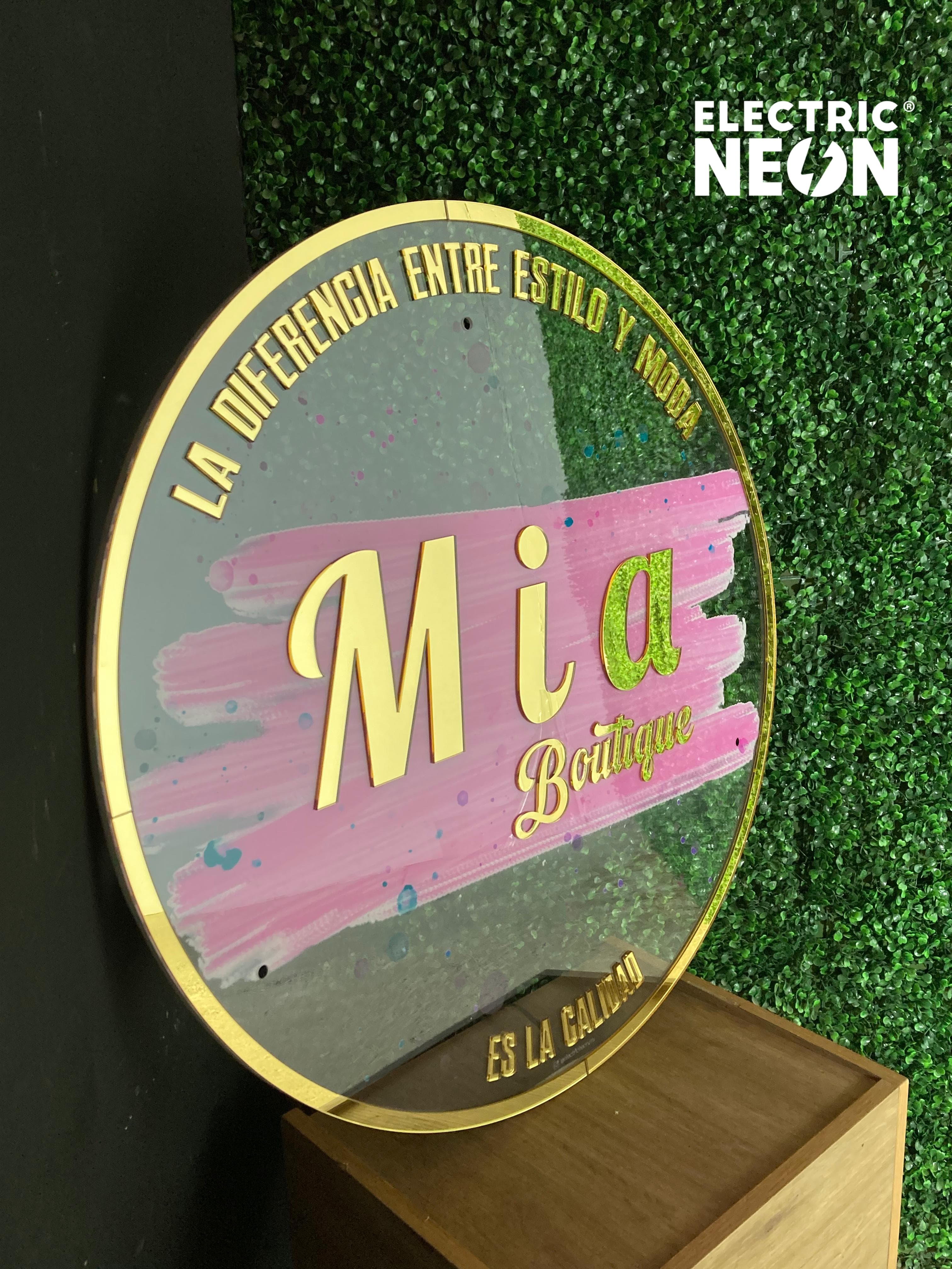 Round sign with 'Mia Boutique' and Spanish text, against a green leafy background.