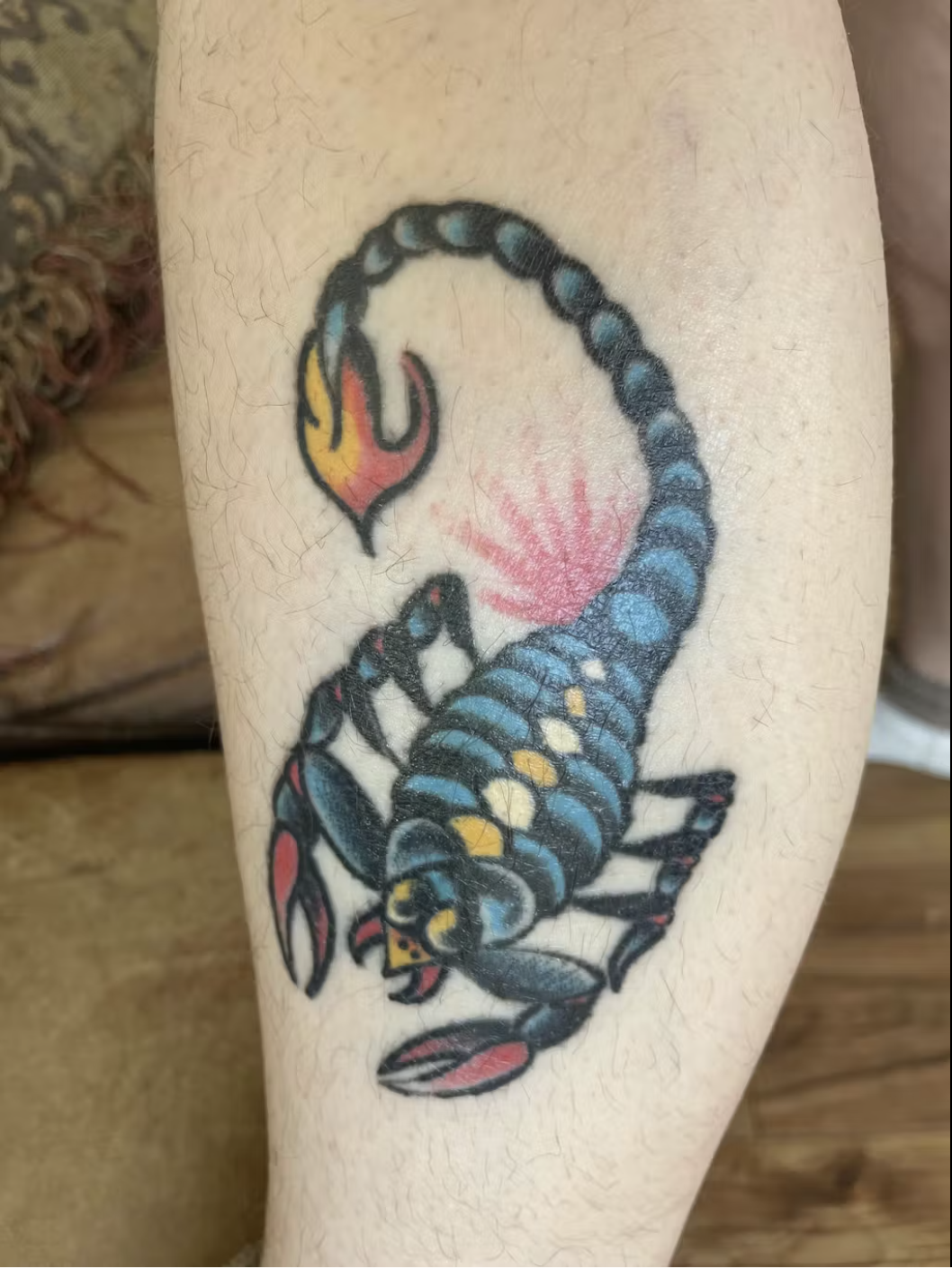 A colorful traditional-style tattoo of a blue and black scorpion on a person's skin.