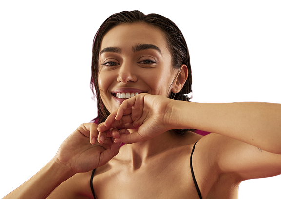 A close-up of a smiling woman with wet hair, holding her hand near her mouth against a black background.