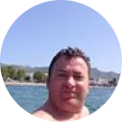 Man in water with mountains and trees in background.