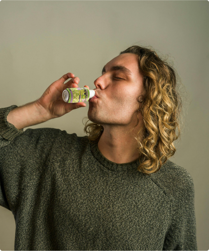 Person with long hair drinking from a small bottle.