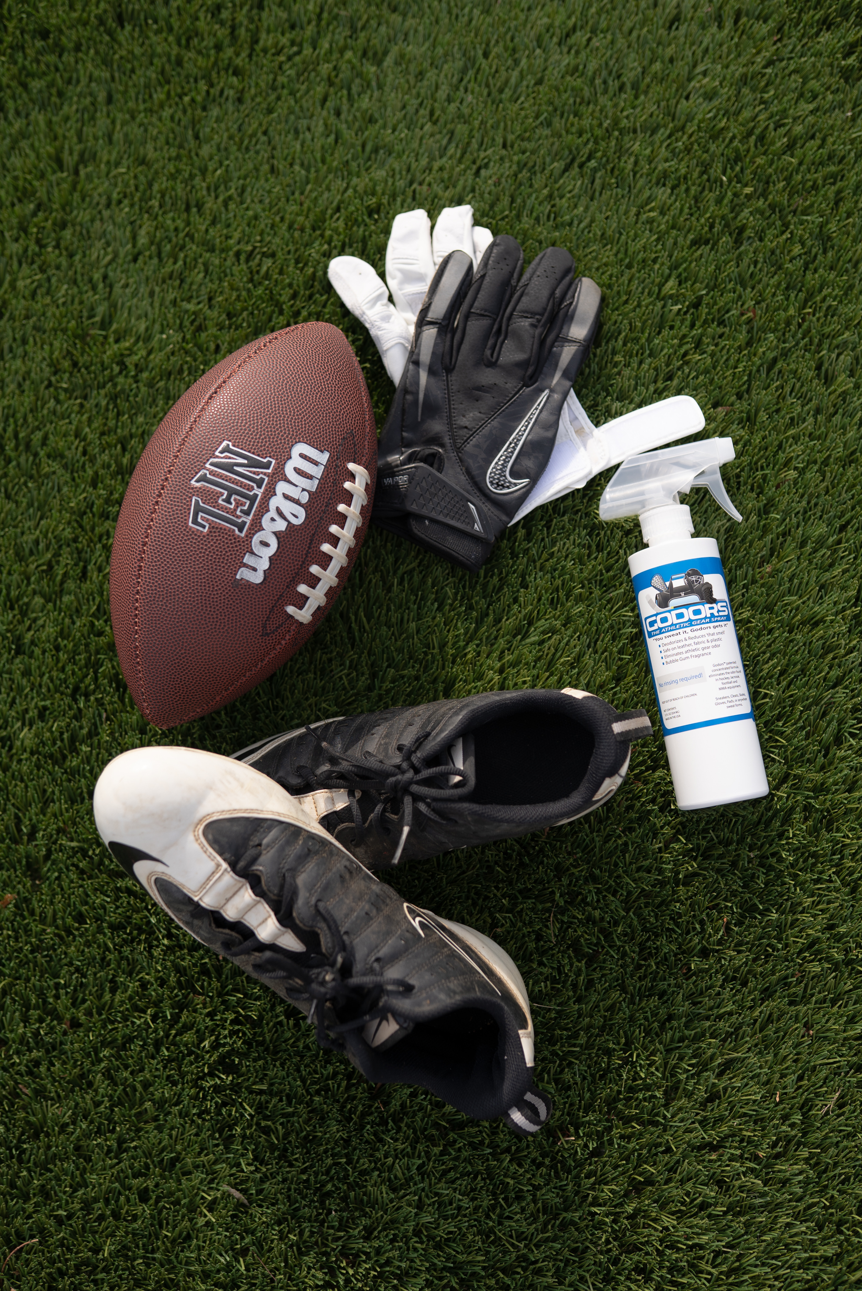 An overhead view of football equipment, including a ball, cleats, gloves, and spray, on artificial turf.