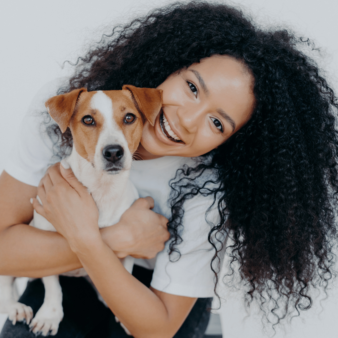Person hugging a small, brown and white dog, both smiling at the camera.