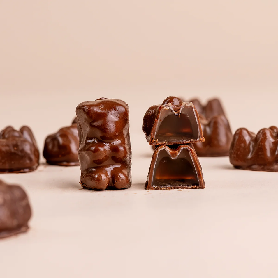Chocolate-covered, bear-shaped candies, with one cut in half to show the gooey filling inside.