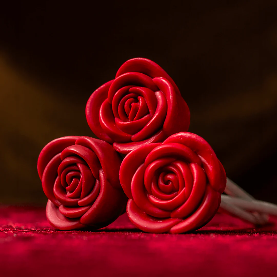 A close-up of three sculpted, artificial red roses lying on a red textured surface with a dark background.