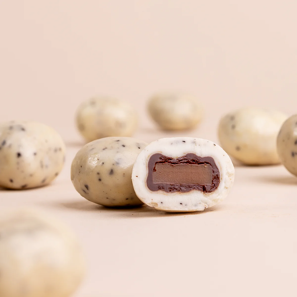 A close-up of speckled white candies with a chocolate filling, one of which is cut in half.