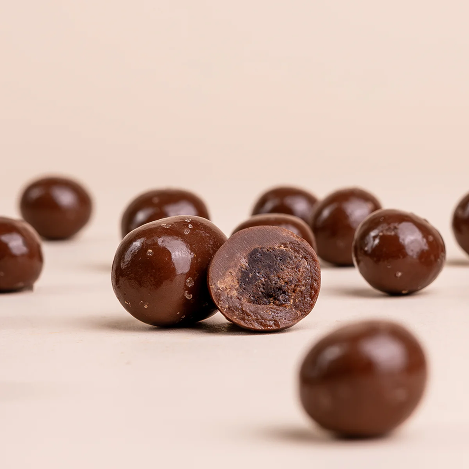 A close-up of round, chocolate-covered candies, with one cut in half to reveal its dark center.