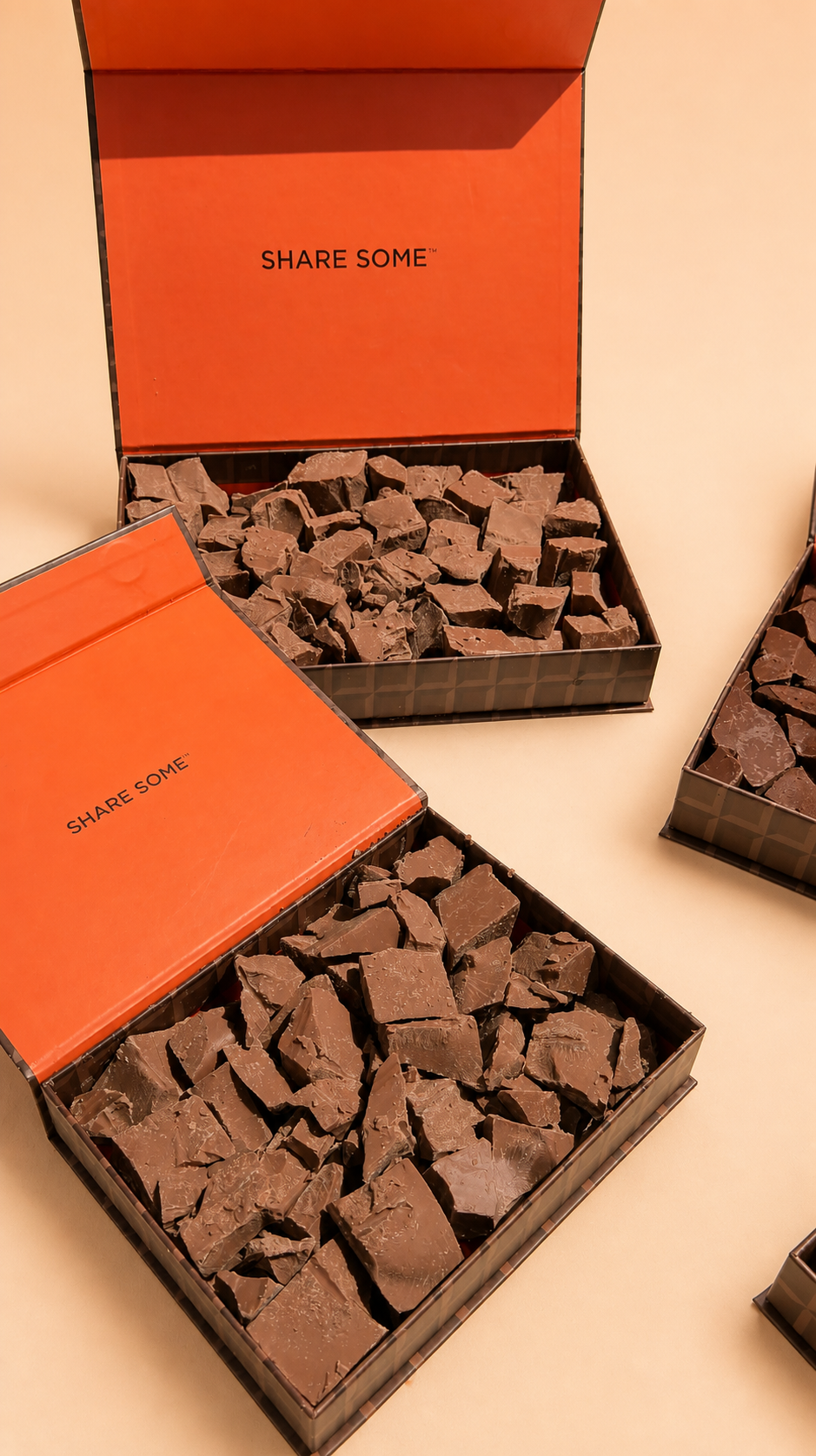 Two open boxes with orange lids filled with large, broken chunks of milk chocolate on a tan surface.