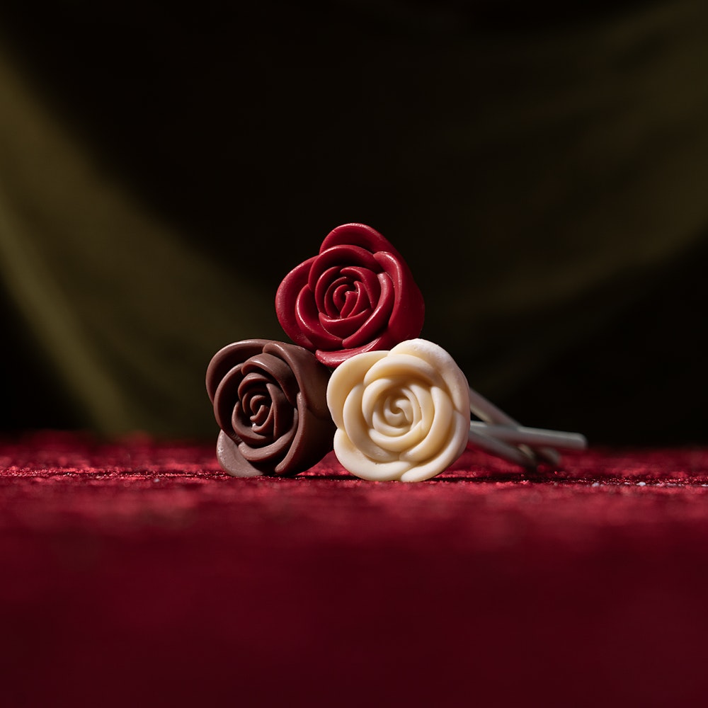 Three chocolate roses in red, dark brown, and white on a textured red surface.