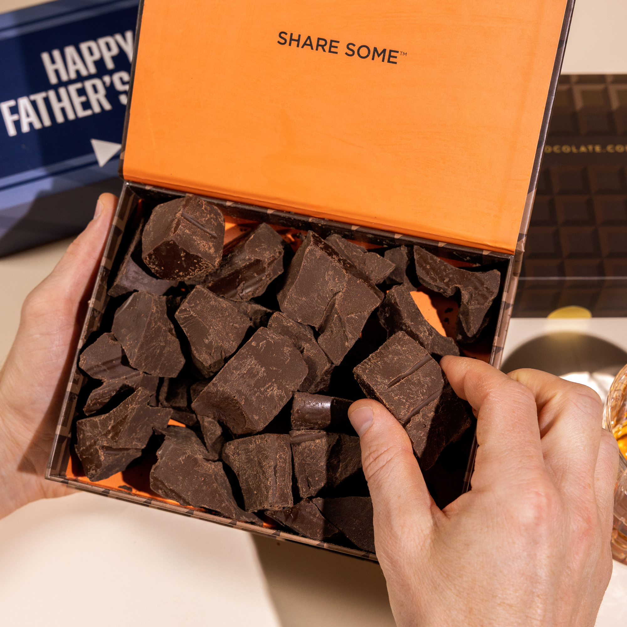A person holds open a gift box of dark chocolate chunks with a Happy Father's Day card behind it.