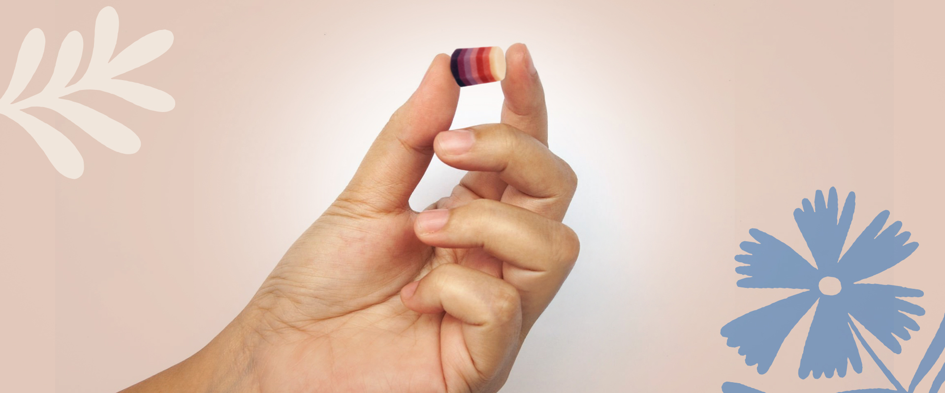Hand holding a small, colorful object with decorative floral elements in the background.