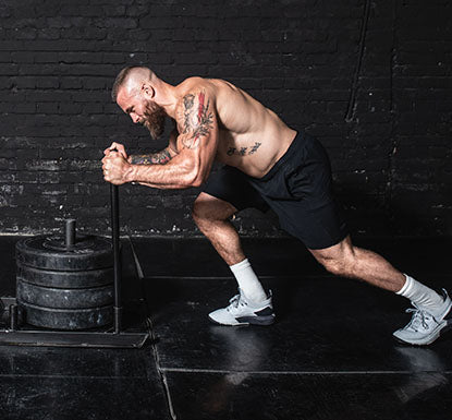 Man pushing a weighted sled in a gym.