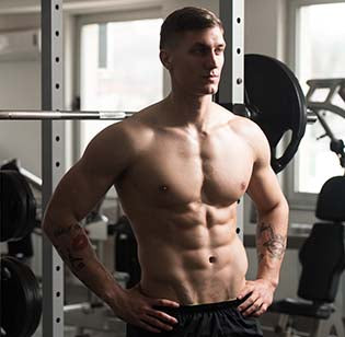 Muscular man standing in a gym next to weightlifting equipment.