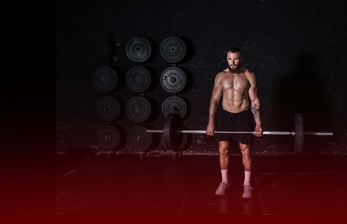 Man lifting a barbell in a gym with weights on the wall.