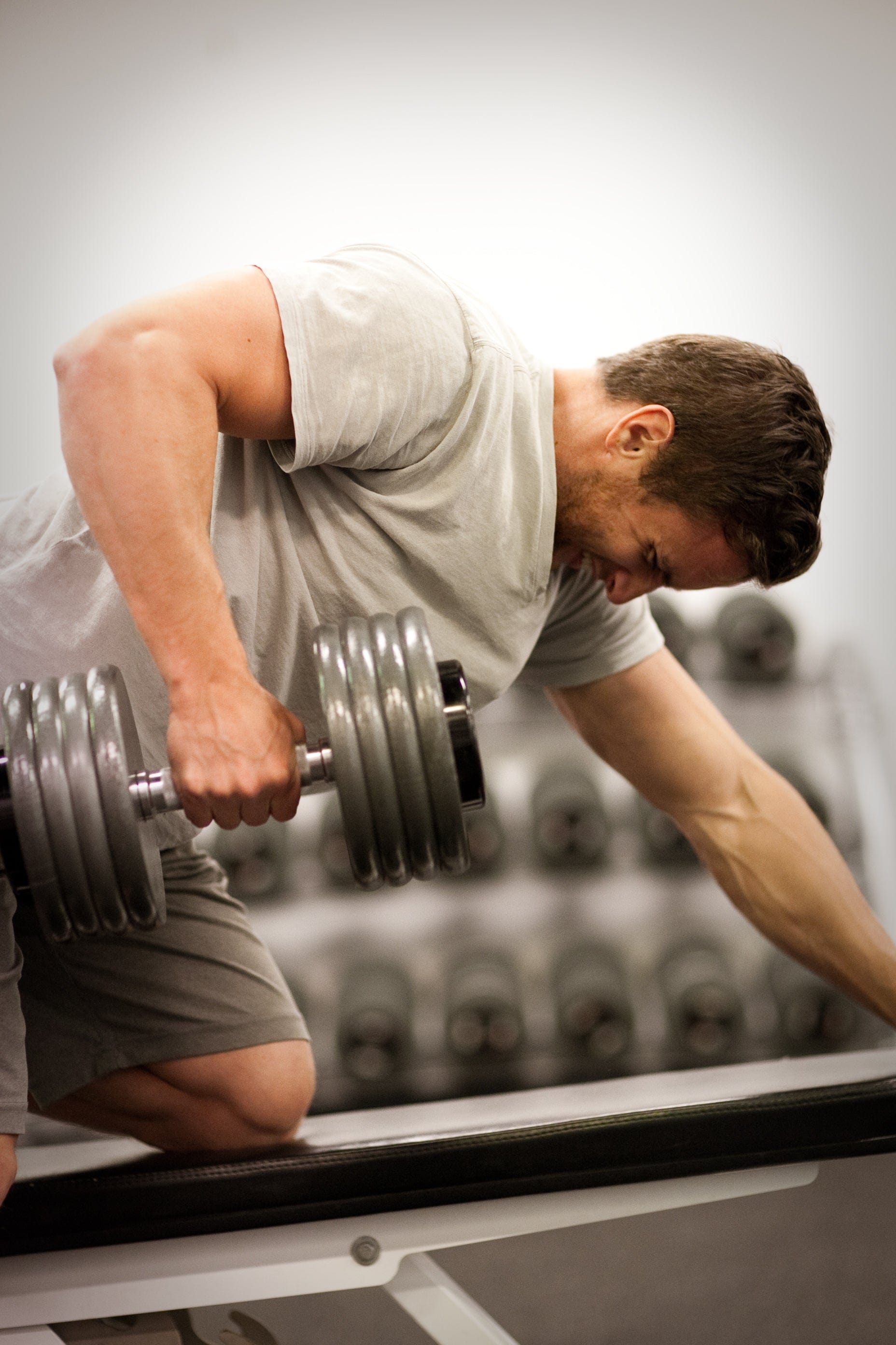 Person lifting a dumbbell while kneeling on a bench in a gym.