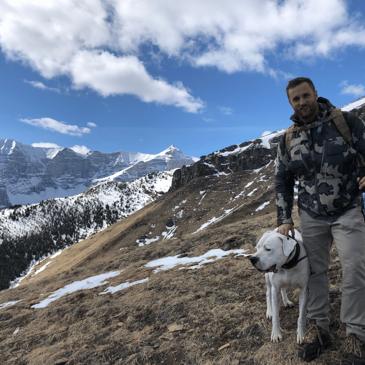 Man with a dog on a snowy mountain trail.